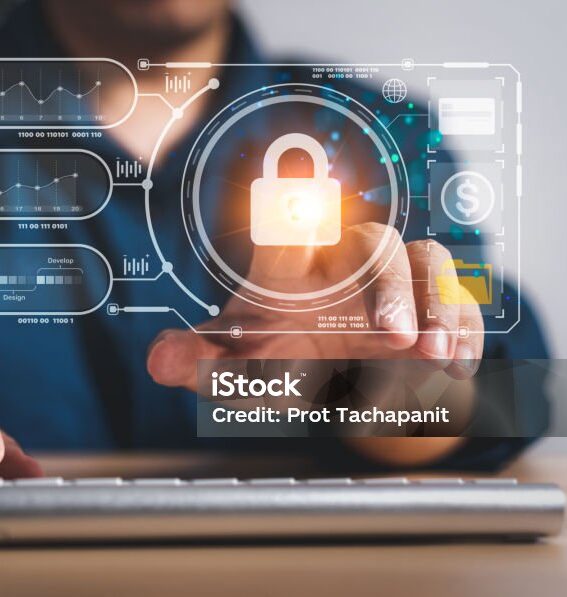 Person arbeitet an einer Computertastatur, während ein holografisches Sicherheitssymbol mit einem Schloss sowie digitale Diagramme und Icons angezeigt werden – Symbol für Cybersicherheit und Datenschutz.